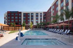 an outdoor swimming pool with lounge chairs and umbrellas next to the hotel's entrance