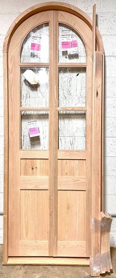 an arched wooden door with glass inserts on the top and bottom panels, in front of a white brick wall