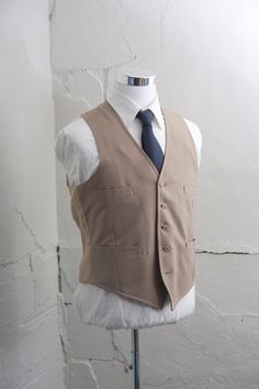 "This vintage vest is a solid khaki color. It has 5 buttons, 4 pockets, and no adjustable back. The wrinkles will release nicely with a good steaming or dry cleaning. NOTE: There is some staining on the back of the vest it is pictured.  Size:  * Chest: 42\" * Length: 22.5\" {measured on the back}  All measurements are taken with garments lying flat. Check out our Additional Policies & FAQ section for detailed sizing information: https://www.etsy.com/shop/BrightWall/policy?ref=shopinfo_policies Classic Tailored Vest With Buttons, Solid Vest With Pockets For Workwear, Fitted Beige Business Vest, Fitted Beige Vest For Business, Classic Single-breasted Sleeveless Vest, Classic Sleeveless Single-breasted Blazer, Beige Single Breasted Sleeveless Vest, Beige Single-breasted Sleeveless Vest, Beige Sleeveless Single-breasted Vest