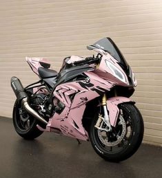 a pink motorcycle parked in front of a brick wall