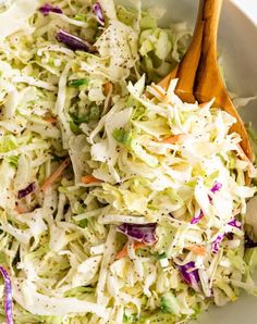 a white bowl filled with coleslaw slaw and wooden spoon in the bowl