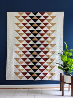 a large quilt hanging on the wall next to a potted plant in front of it