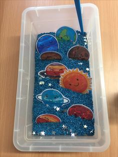 a plastic container filled with magnets on top of a wooden table next to a blue straw