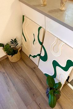 two green plants are sitting on the floor in front of some white cabinets and countertops