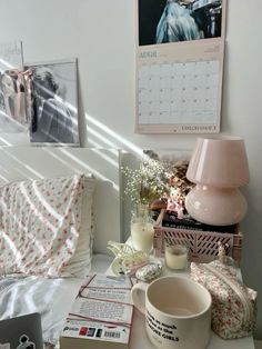 a white bed topped with lots of pillows next to a pink lamp