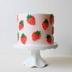 a pink cake with strawberries on it sitting on a white pedestal next to a wall