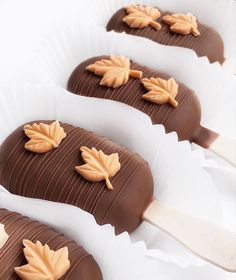 four chocolate covered candys with leaves on them sitting in white paper trays, ready to be eaten