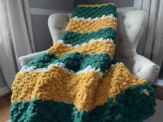 a green, yellow and white crocheted blanket sitting on top of a chair