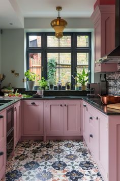 a kitchen with pink cabinets and black counter tops is pictured in this image, there are potted plants on the window sill