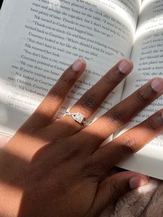 a person's hand holding an open book with a diamond ring on top of it