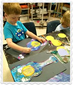 two young boys sitting at a table working on paper art projects with scissors and glue