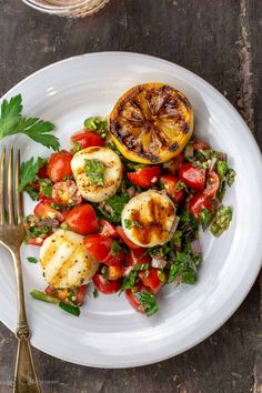 a white plate topped with scallops, tomatoes and lettuce next to a fork