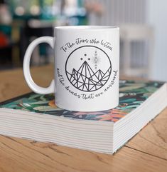 a white coffee mug sitting on top of a wooden table next to a paperback book