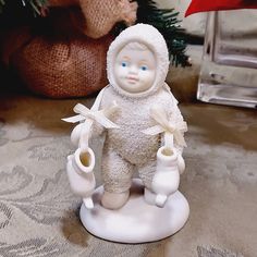 a small white figurine holding two mugs in front of a christmas tree