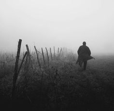 a person walking in the fog with a coat over their shoulders and an open field behind them