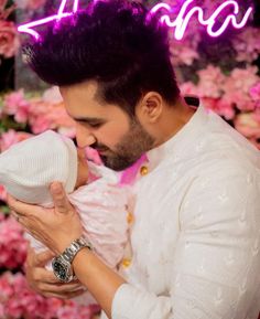 a man holding a baby in his arms with the neon sign above him that reads i love you