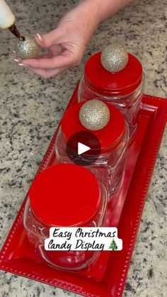 a red tray holding three empty glass jars with silver glitter balls on them and the words easy christmas candy dispenser