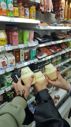 two people holding up cups in front of a store shelf filled with milk and other items