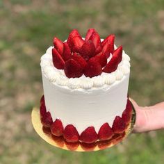 a hand holding a white cake with strawberries on top and frosting in the middle