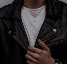 a man wearing a black leather jacket and white t - shirt is holding his watch