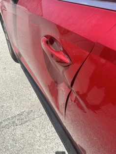 a red car parked on the street with it's door partially open and its handle missing