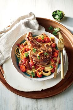 a white plate topped with pasta and meat covered in tomato sauce on top of a wooden tray