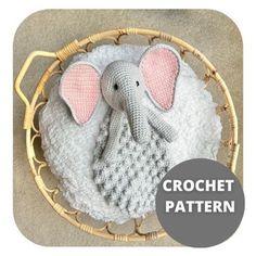 an elephant knitted in grey and pink sits on a white blanket inside a wicker basket