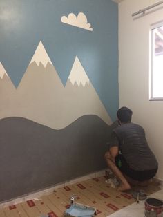 a man is painting a mountain mural on the wall