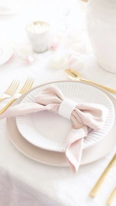 a table set with white plates and pink napkins, gold forks and silverware