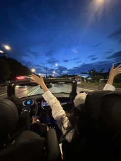 two people are driving down the road at night with their hands up in the air