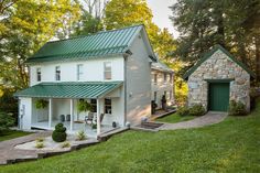 a white house with a green roof in the middle of some trees and grass,