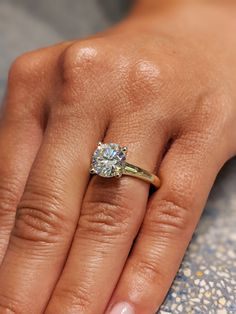 a woman's hand with a diamond ring on top of her finger and the other hand holding an engagement ring