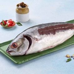 a fish is sitting on a green plate next to some nuts and other food items