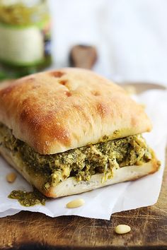 a sandwich with pesto and cheese is on a piece of paper next to a jar