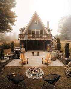 an outdoor fire pit in front of a house on a foggy day with chairs around it