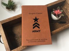 an army book sitting on top of a wooden tray next to a flower pot and pen