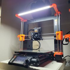 an orange and black 3d printer sitting on top of a white table next to a light