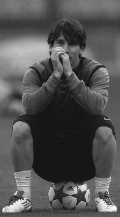 a man sitting on top of a soccer ball holding his hands to his face while covering his mouth