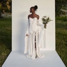 a woman standing in front of a white backdrop wearing a dress and holding a bouquet