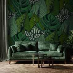 a green couch sitting in front of a wall with leaves on it's side