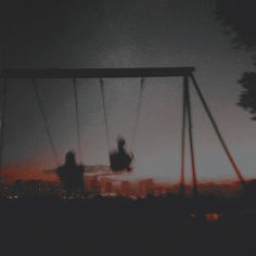 two people sitting on swings at night with the city lights in the backgroud