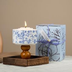 a lit candle sitting on top of a wooden stand next to a blue and white box