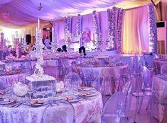 a room filled with lots of tables and chairs covered in purple cloths, decorated with crystal chandeliers