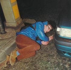 a man sitting on the ground next to a car looking at his hand in front of him