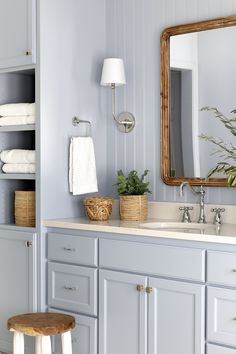 a bathroom with gray cabinets and white towels on the shelf, along with a wooden stool