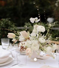 an arrangement of white flowers in a vase on a table with place settings and utensils