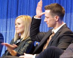 two people sitting next to each other in front of a blue curtain with their hands up