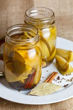 three jars filled with pickles and spices on a white plate next to a spoon