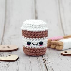 a crocheted coffee cup sitting on top of a wooden table next to buttons