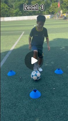 a young boy kicking a soccer ball on top of a field with blue cones in front of him